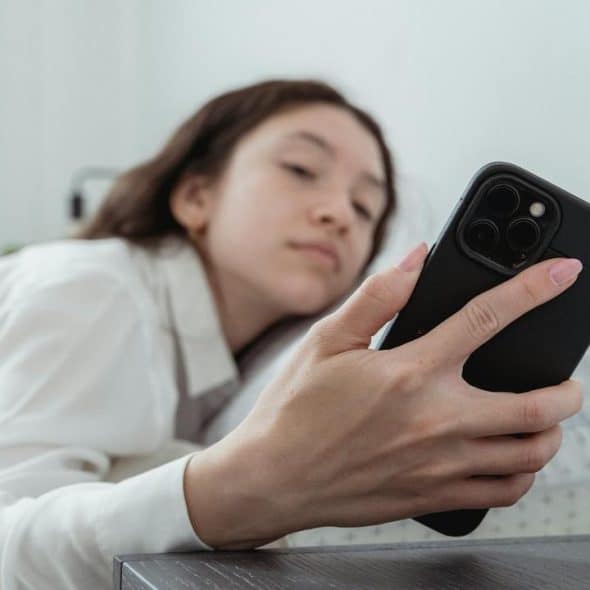 A woman lying on a bed, looking at her smartphone.