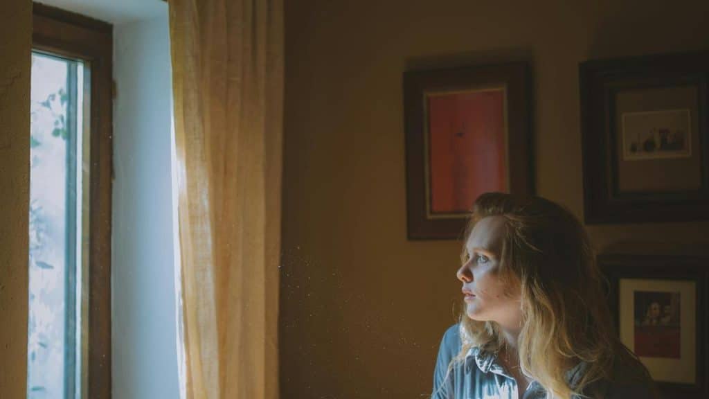 A woman sitting by a window looking outside thoughtfully.