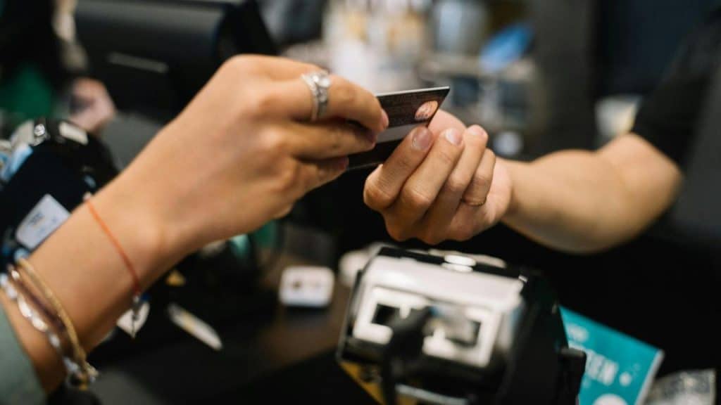 A person handing a credit card to another person at a checkout counter.