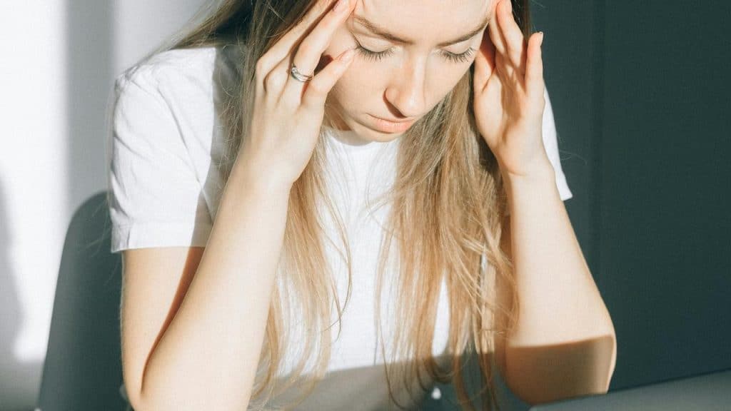 A woman sitting with her head down and hands on her temples looking stressed.