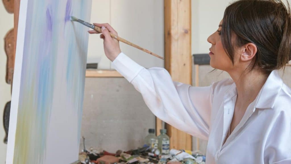 A woman painting on a canvas with a brush in an art studio.