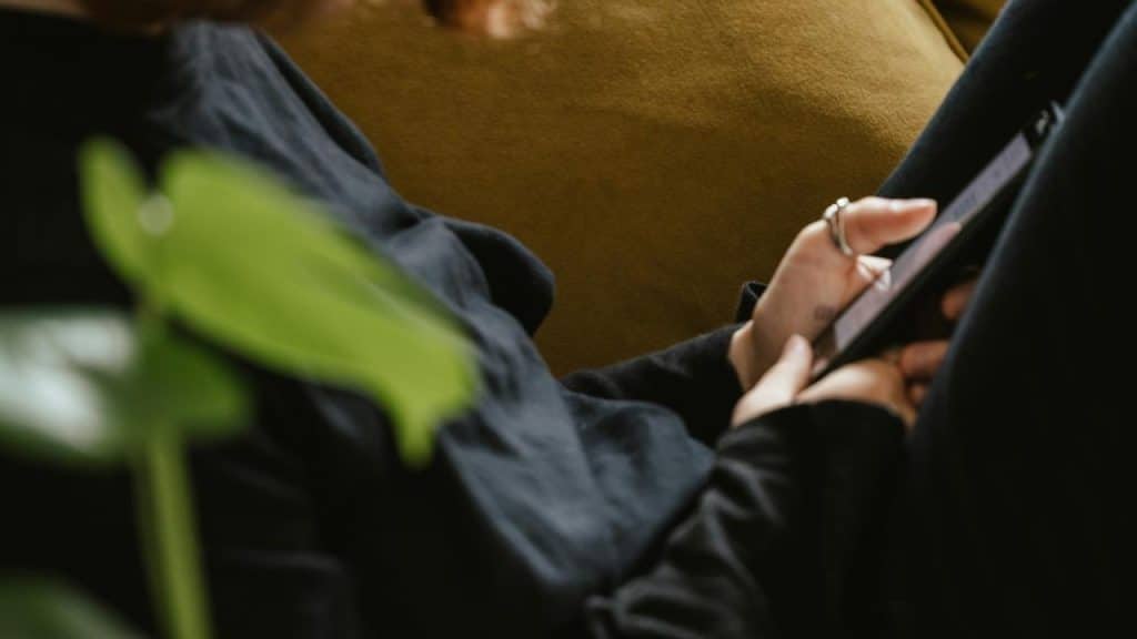 A person holding and using a tablet while sitting indoors.