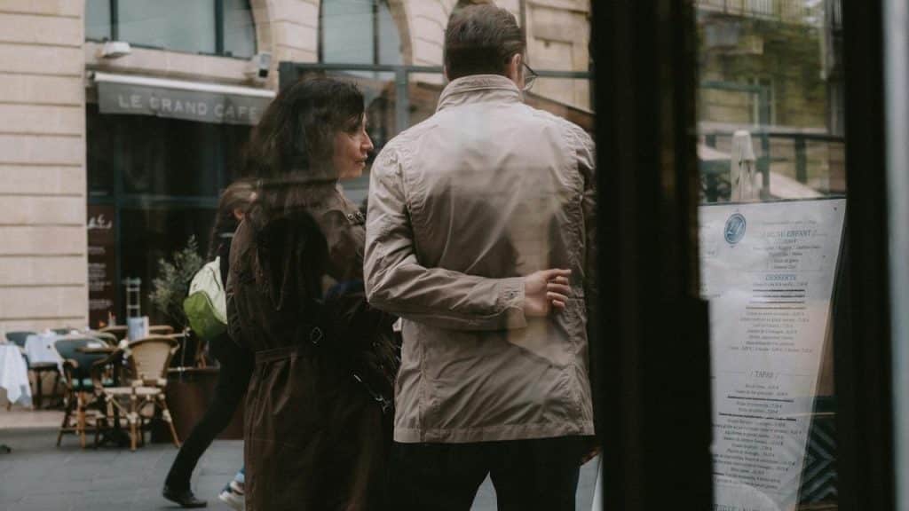 A couple standing close together outside a café, seen through a window.