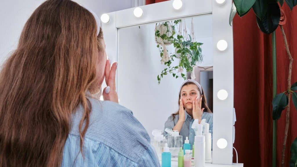 A woman applying skincare while looking in a lighted vanity mirror.Date night? You'll spend an hour getting ready: hair done, makeup on point, outfit carefully chosen. But around the house when it's just him? Stained sweatpants, hair in a messy bun for the third day straight, zero effort. And yeah, comfort matters. But when the only time you put in effort is when other people will see you, he notices.