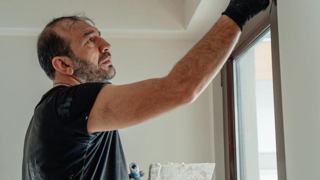 A man applying plaster to the wall above a window during renovation.