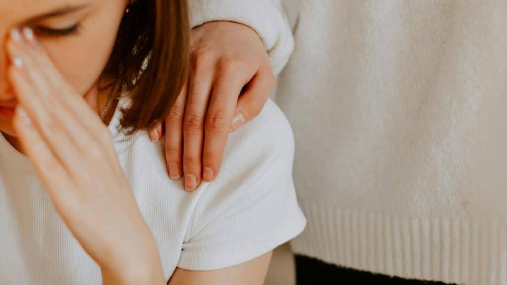 A hand resting gently on a person’s shoulder in a comforting gesture.