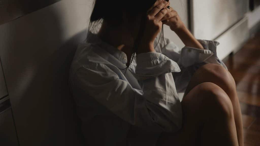 A person sitting on the floor by a wall with their head in their hands.