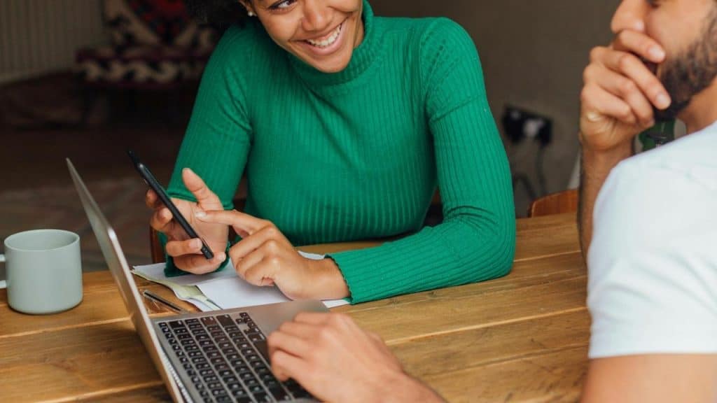 A woman smiling while showing something on her phone to a man at a table.