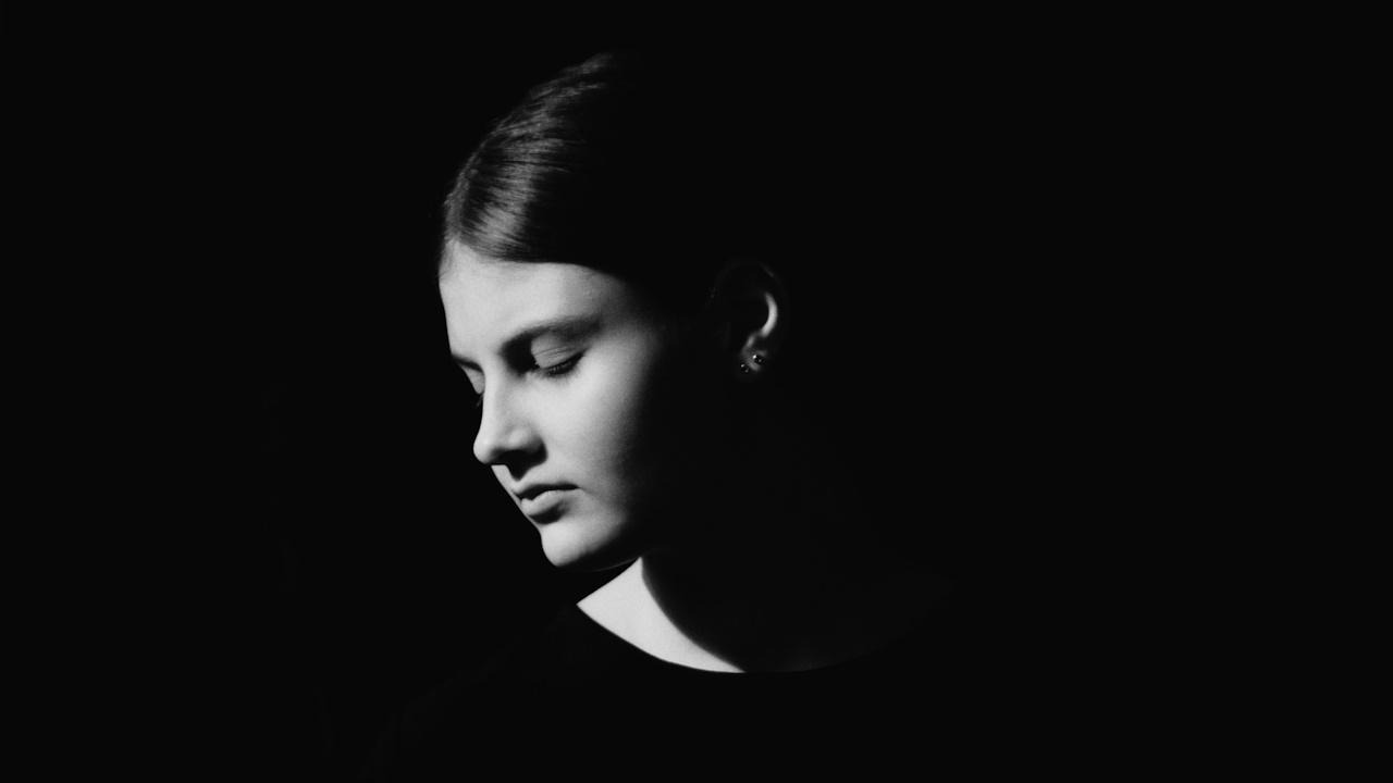 A young woman holding flowers in dramatic lighting.