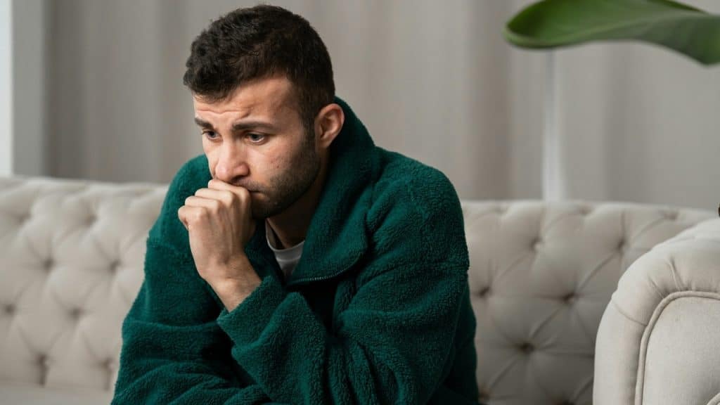 Close-up of a man in a green fleece sitting on a sofa with hand to mouth.