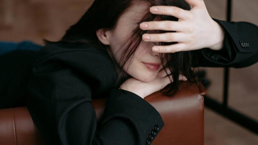A woman in a black blazer resting her head on a chair with her hand partially covering her face.