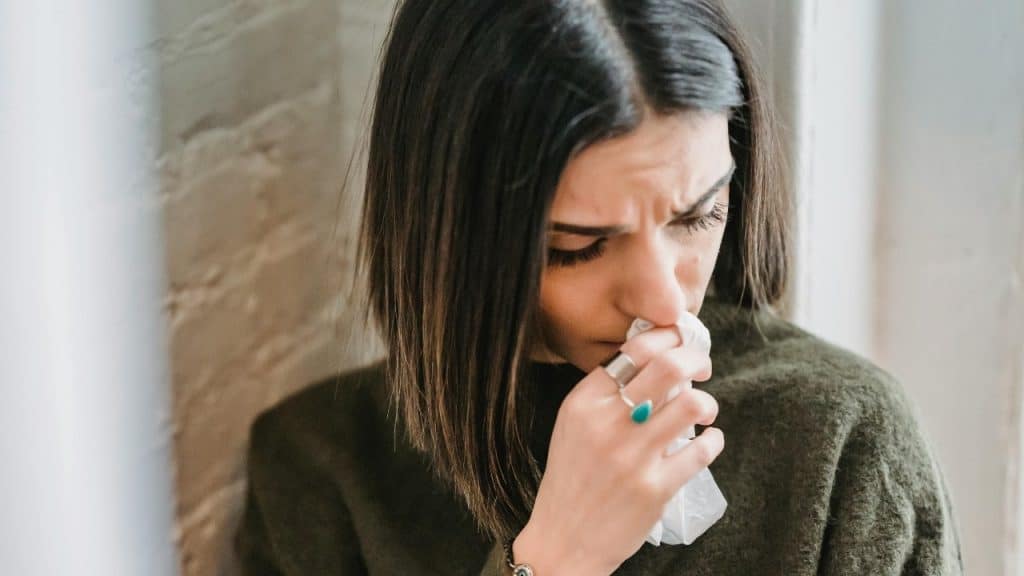 Close-up of a woman with dark hair holding a tissue to her nose and looking down.