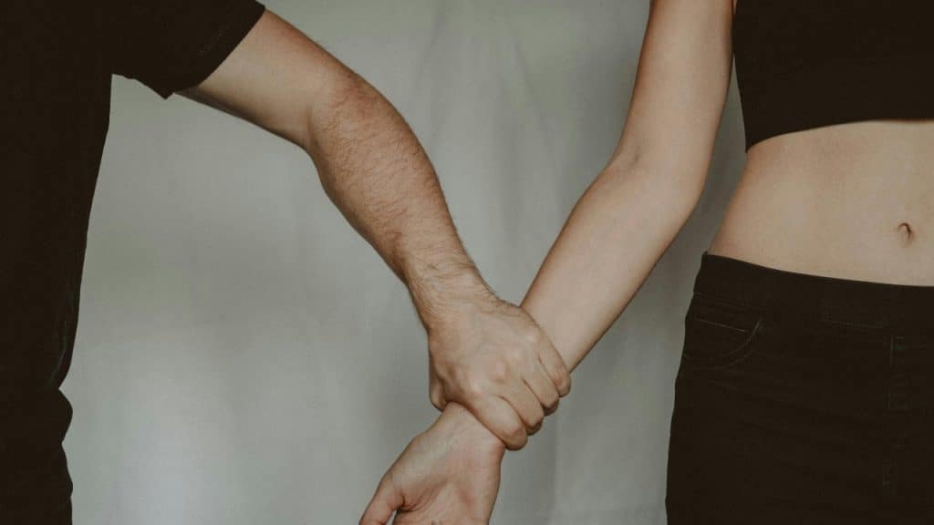 A close-up shot shows one person firmly gripping another person's wrist against a light background.