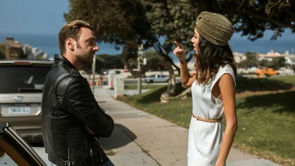 A woman in a gold headpiece points her finger at a man in a jacket.