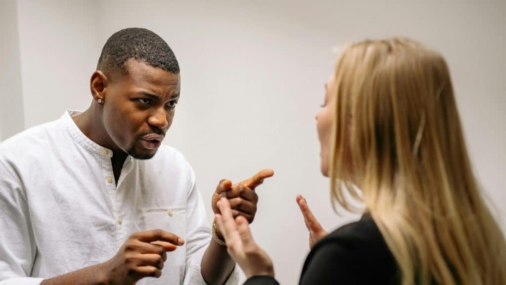 A man in a white shirt points his finger while speaking to a blonde woman.