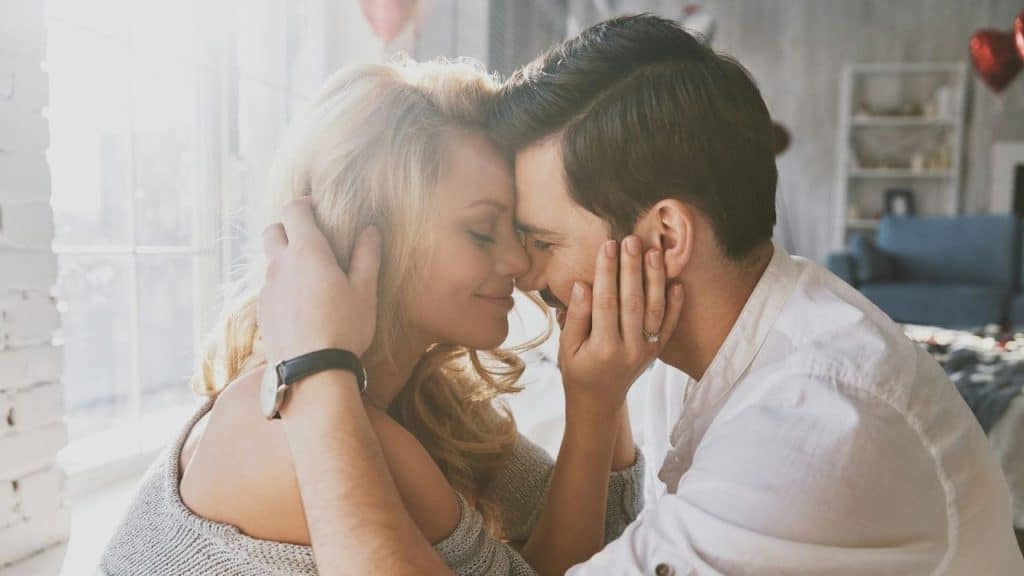 A man and woman touch foreheads and smile while the man holds her face