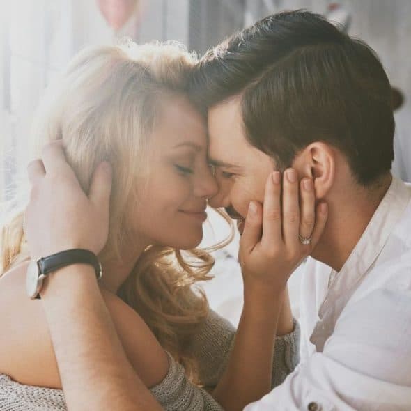 A man and woman touch foreheads and smile while the man holds her face