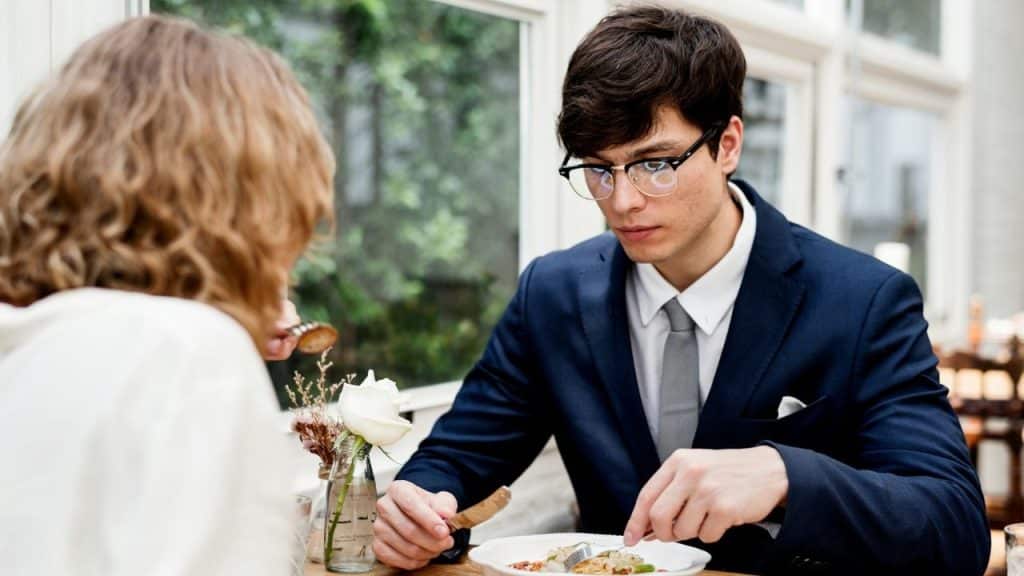 A man in a suit and glasses eats a meal while looking down at his plate.