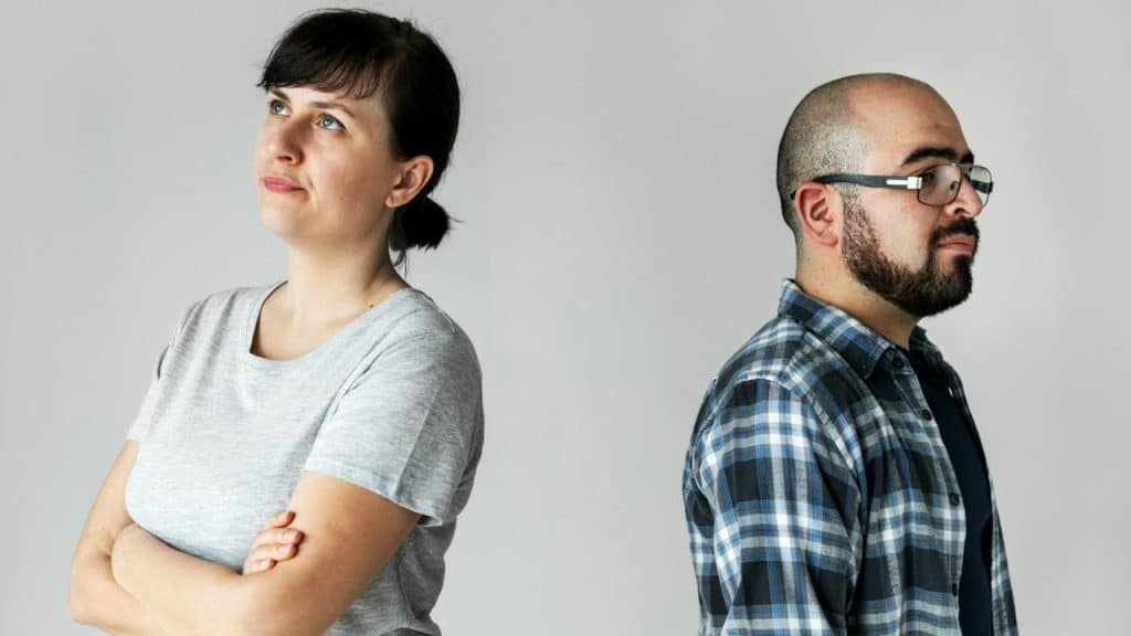 A man and woman stand back-to-back with arms crossed against a plain grey background.