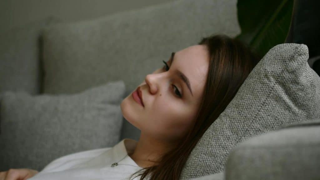 A woman lies on a couch, gazing thoughtfully into the distance.