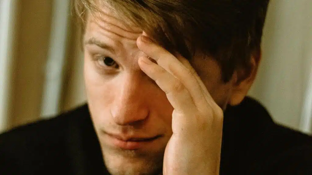 A close-up of a man resting his forehead on his hand with a concerned expression.