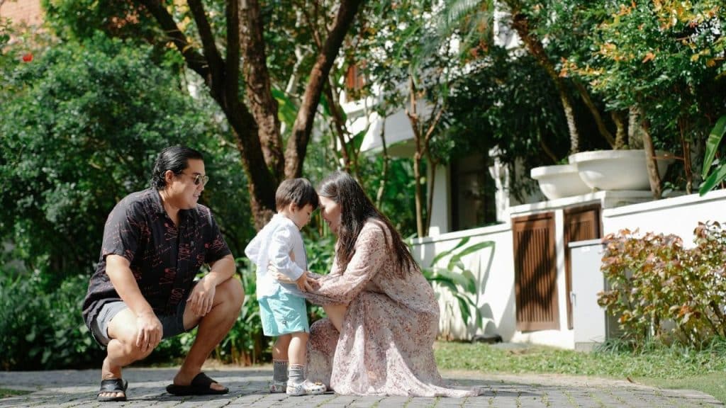A man and woman crouch outdoors on a stone path next to a small child.
