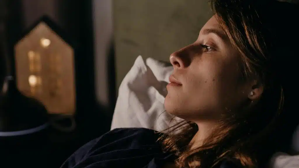 A woman lying in bed at night, gazing thoughtfully into the distance.
