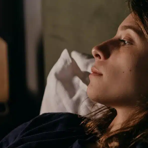 A woman lying in bed at night, gazing thoughtfully into the distance.