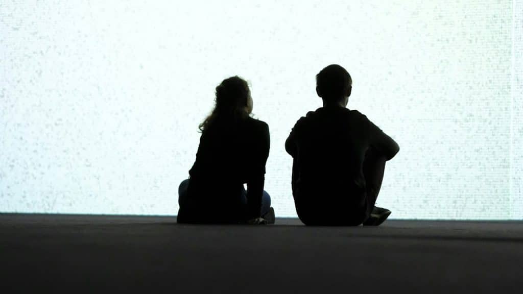 A couple sit and gaze at the bright background.