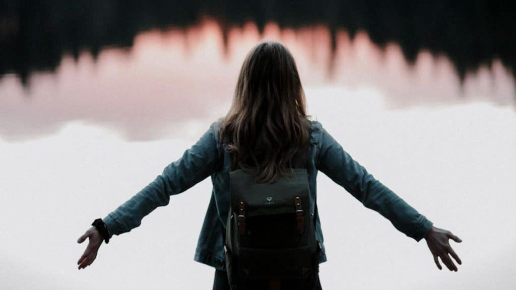 A woman standing with her arms stretched in front of a body of water.