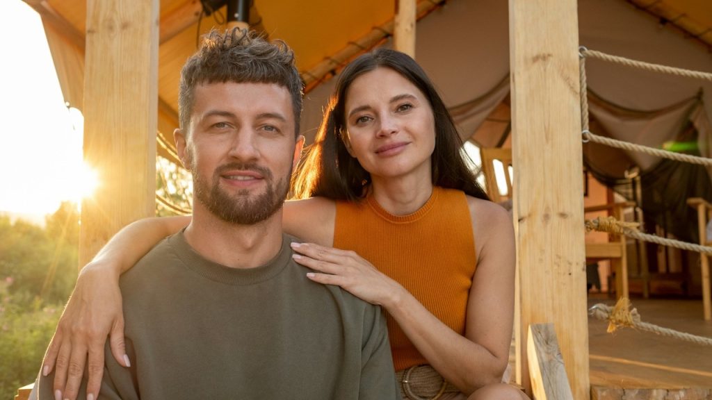 Happy young brunette woman embracing her husband while both enjoy a summer rest by the glamping house.