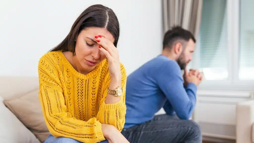 Unhappy, thoughtful, married couple spouses sitting separately on a couch at home.