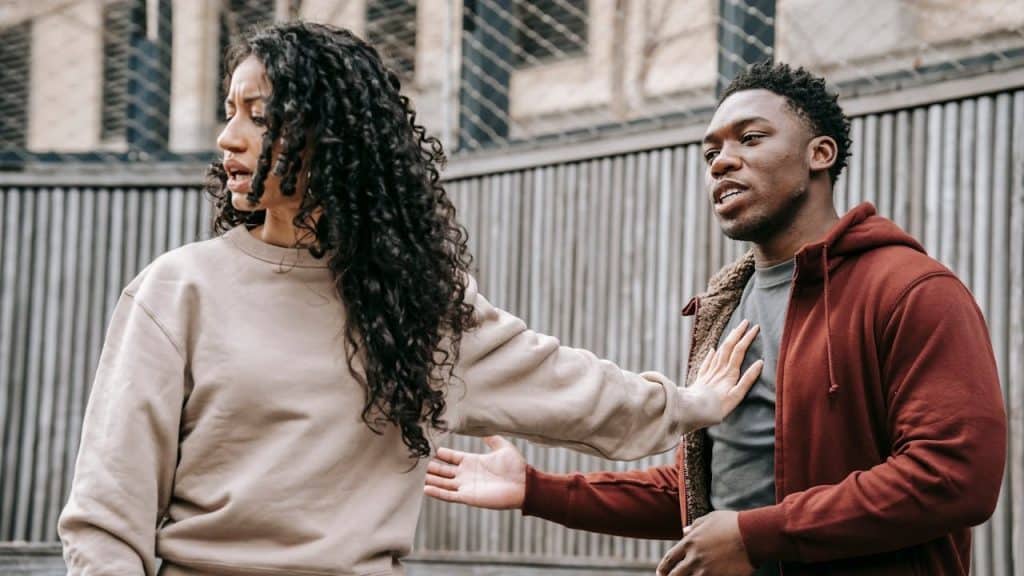 A woman is pushing away a man's hand on her chest during an outdoor argument.