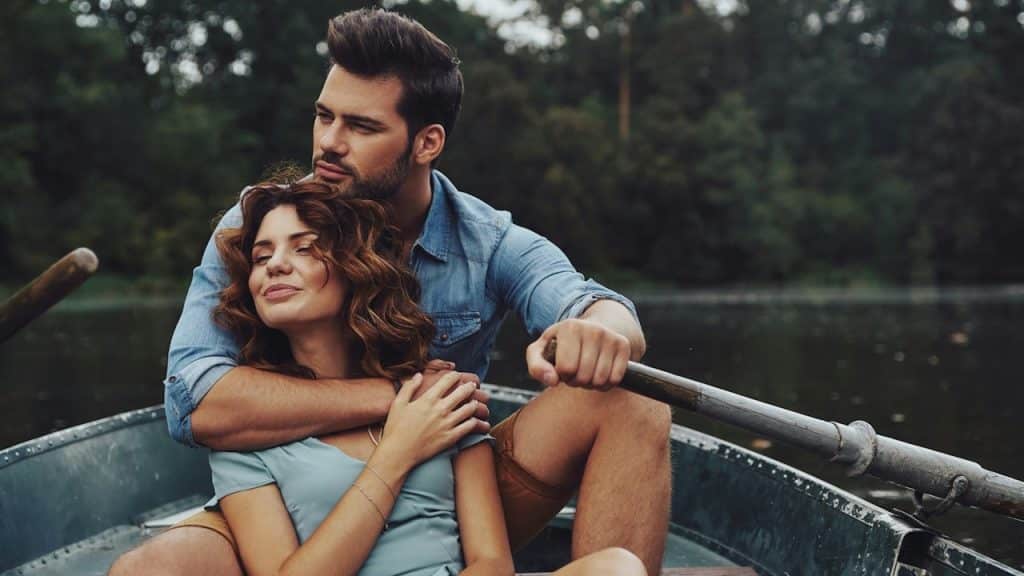 Beautiful young couple embracing and looking away while enjoying a romantic date on the lake.