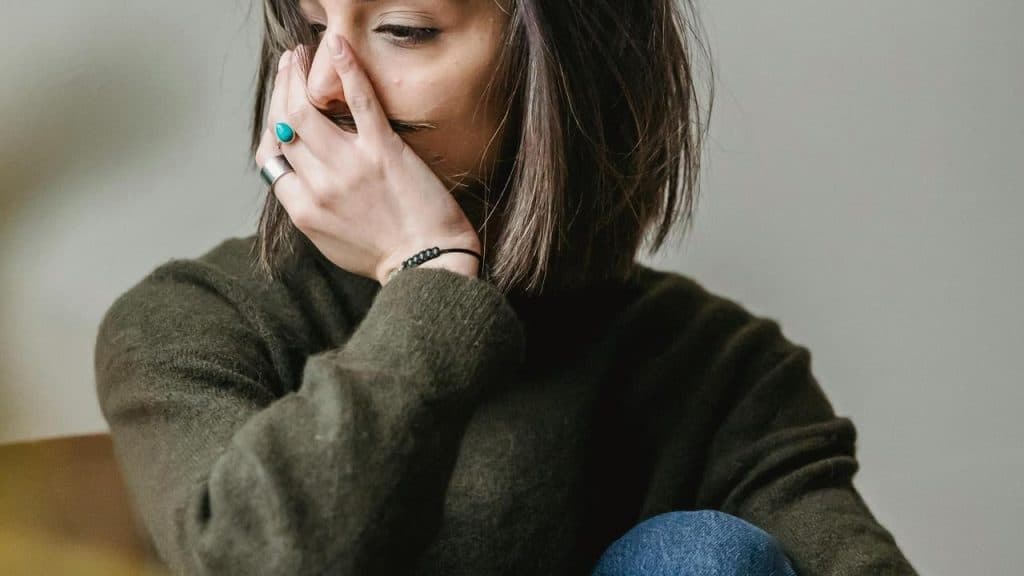 A woman sitting with her hand covering her mouth, looking distressed.
