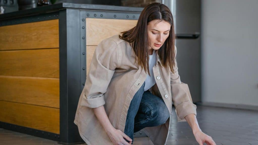 A woman crouching on a kitchen floor, looking down at something out of frame.