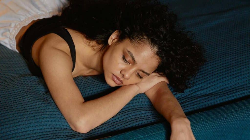 A woman lying on a bed with her arm stretched out, looking tired or sad.