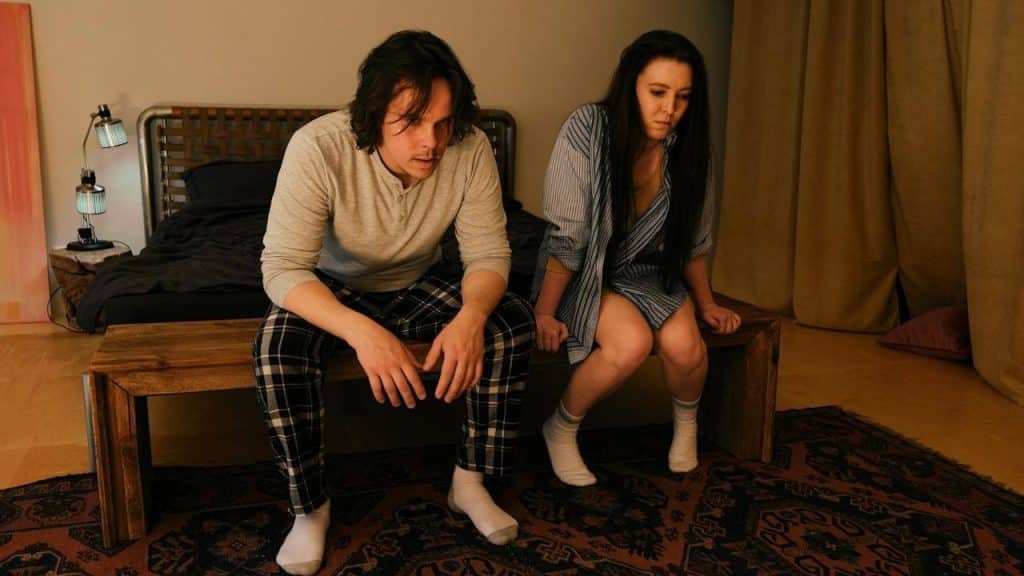 An angry man is sitting with a woman who is feeling frustrated.