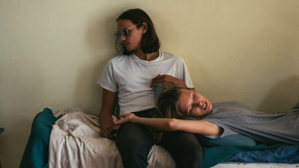 A woman lies across the lap of a man who is wearing sunglasses and looking away.