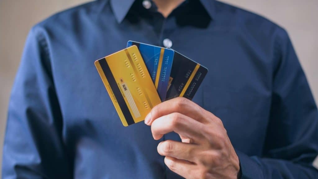 A person in a blue shirt holds three credit cards fanned out in their hand.