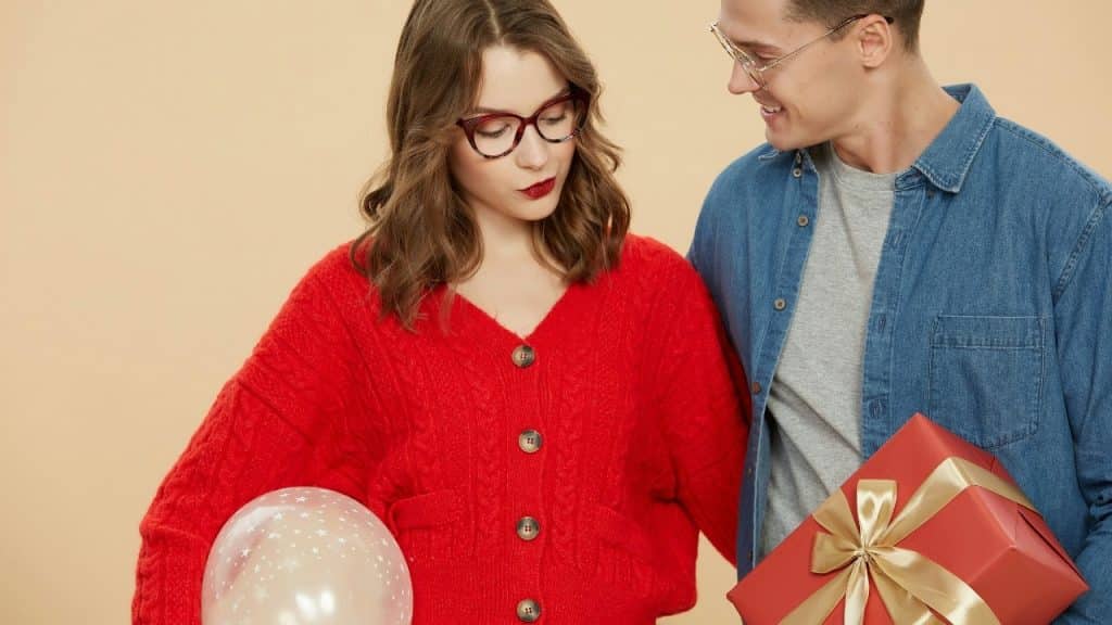 A man holds a gift and balloon while standing next to a woman in red.