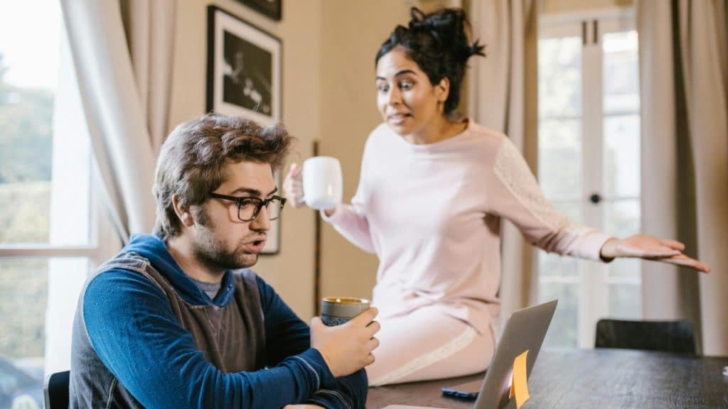 A man sits at a laptop while a woman stands behind him with an open hand.