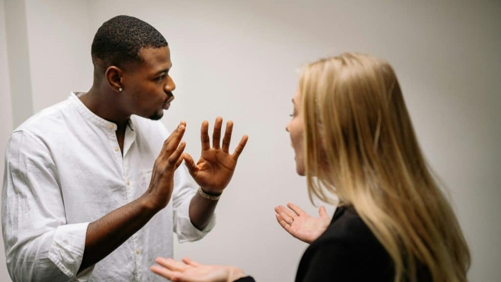 A man in a white shirt holds his hands up while talking to a woman.