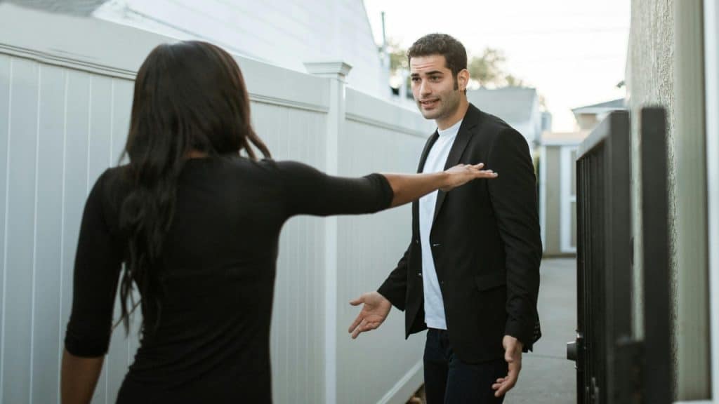 A woman reaches toward a man in a blazer who is gesturing with open hands.