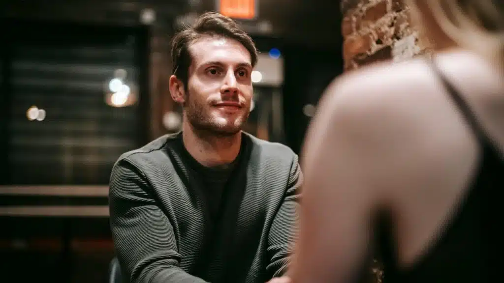 A man in a grey sweater looks toward a woman who is partially out of frame.