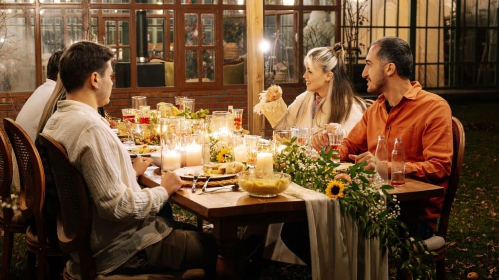 Several people sit around an outdoor dinner table decorated with flowers and lit candles.