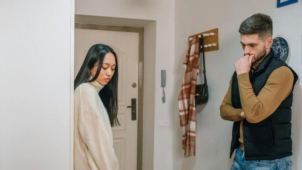 A woman stands in a doorway while a man leans against a wall nearby.