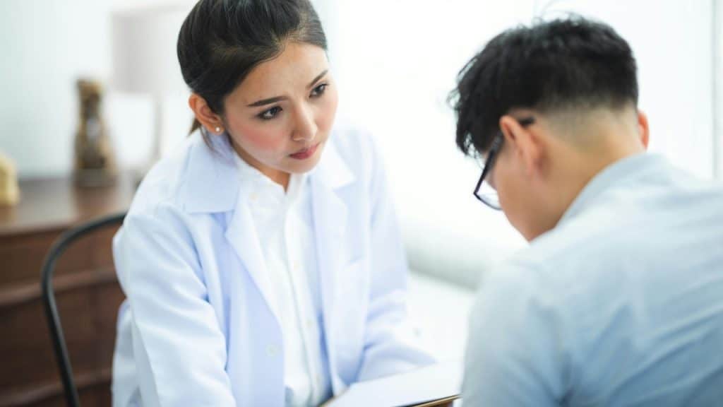 A female doctor in a white coat talks to a man during a medical consultation.