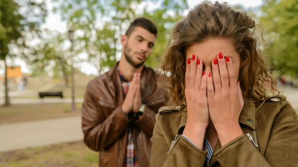A woman covering her face while a man stands behind her