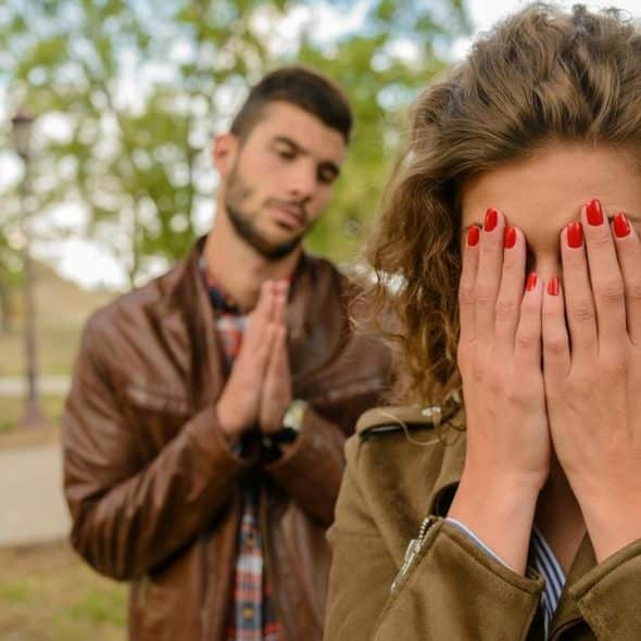 A woman covering her face while a man stands behind her